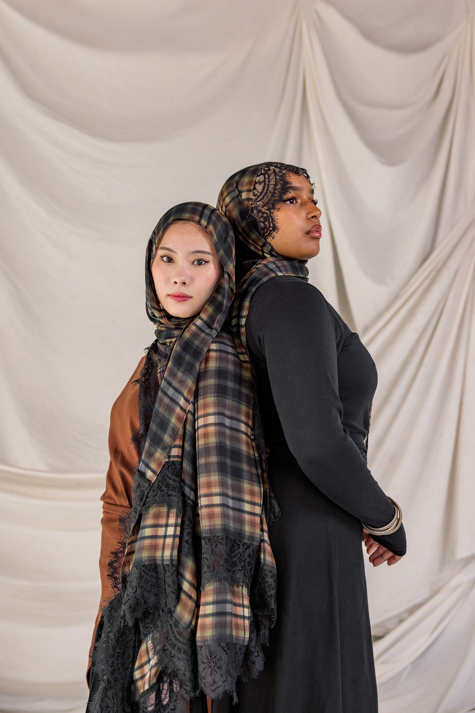 Two women wearing hijabs with plaid patterns against a plain background