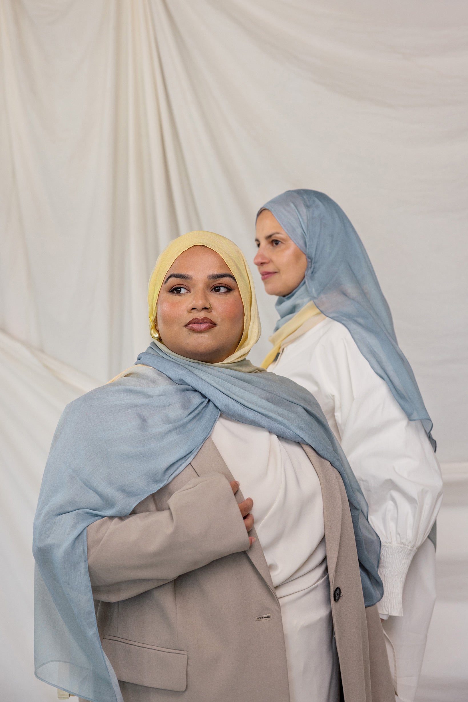 Two women wearing blue / yellow ombre hijabs in front of a plain background