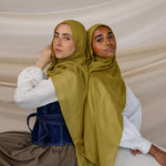 Two models wearing Guava Green hijabs with draping to the side against backdrop.