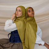 Two models wearing Guava Green hijabs with draping to the side against backdrop.