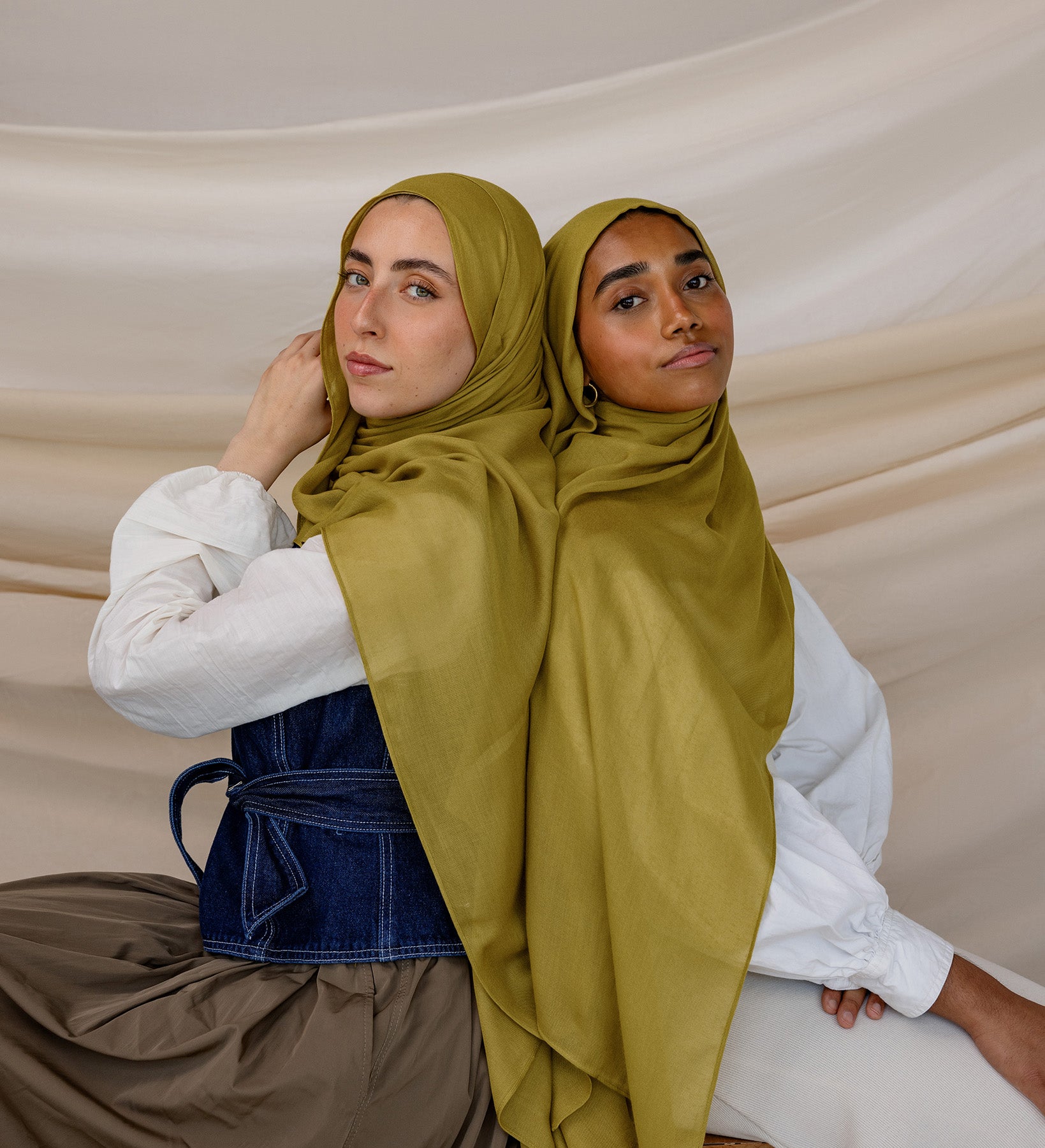 Two models wearing Guava Green hijabs with draping to the side against backdrop.