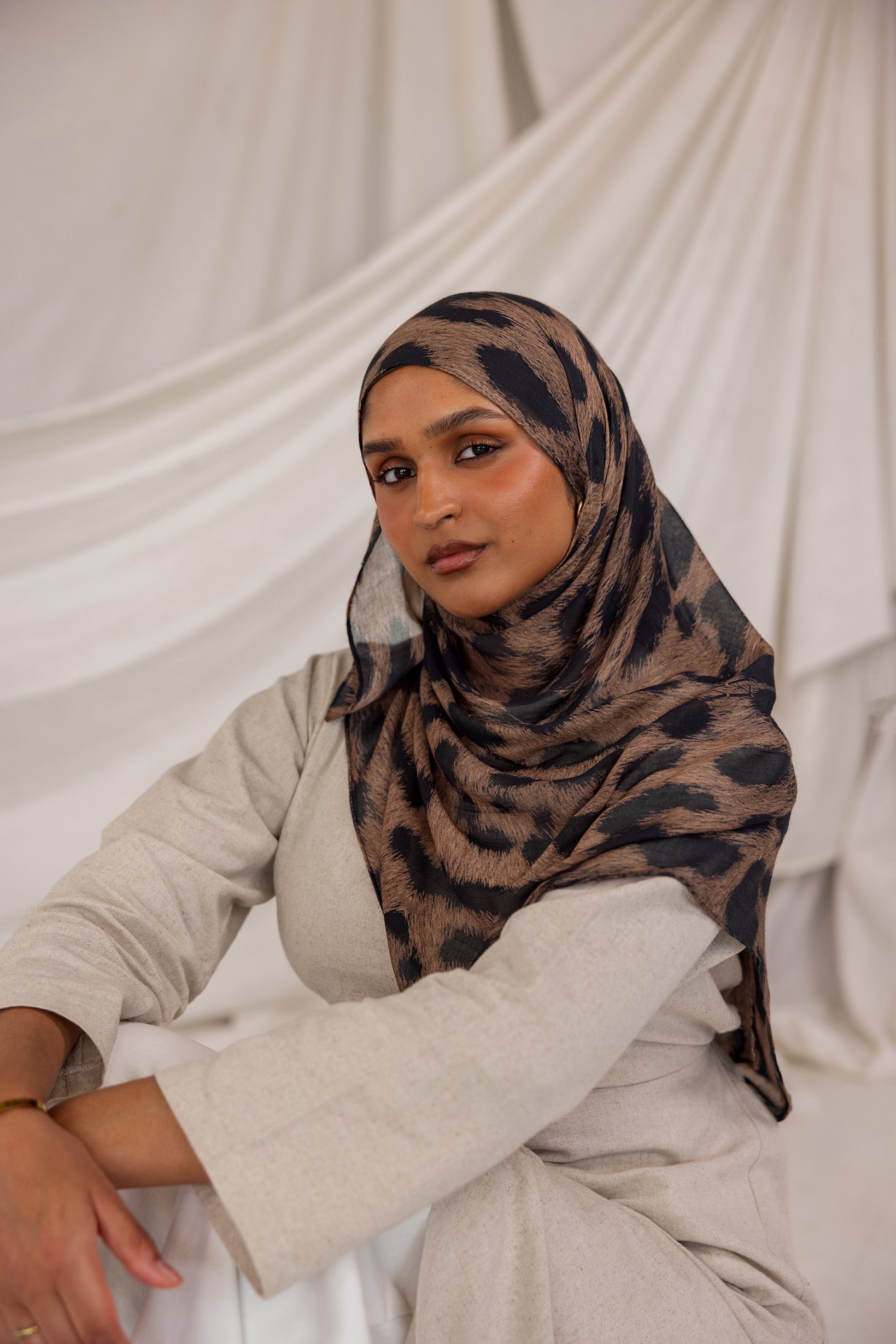 Model styled in a patterned leopard hijab sitting against a white draped background
