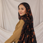 Model wearing a black and brown tortoiseshell patterned hijab against a plain background