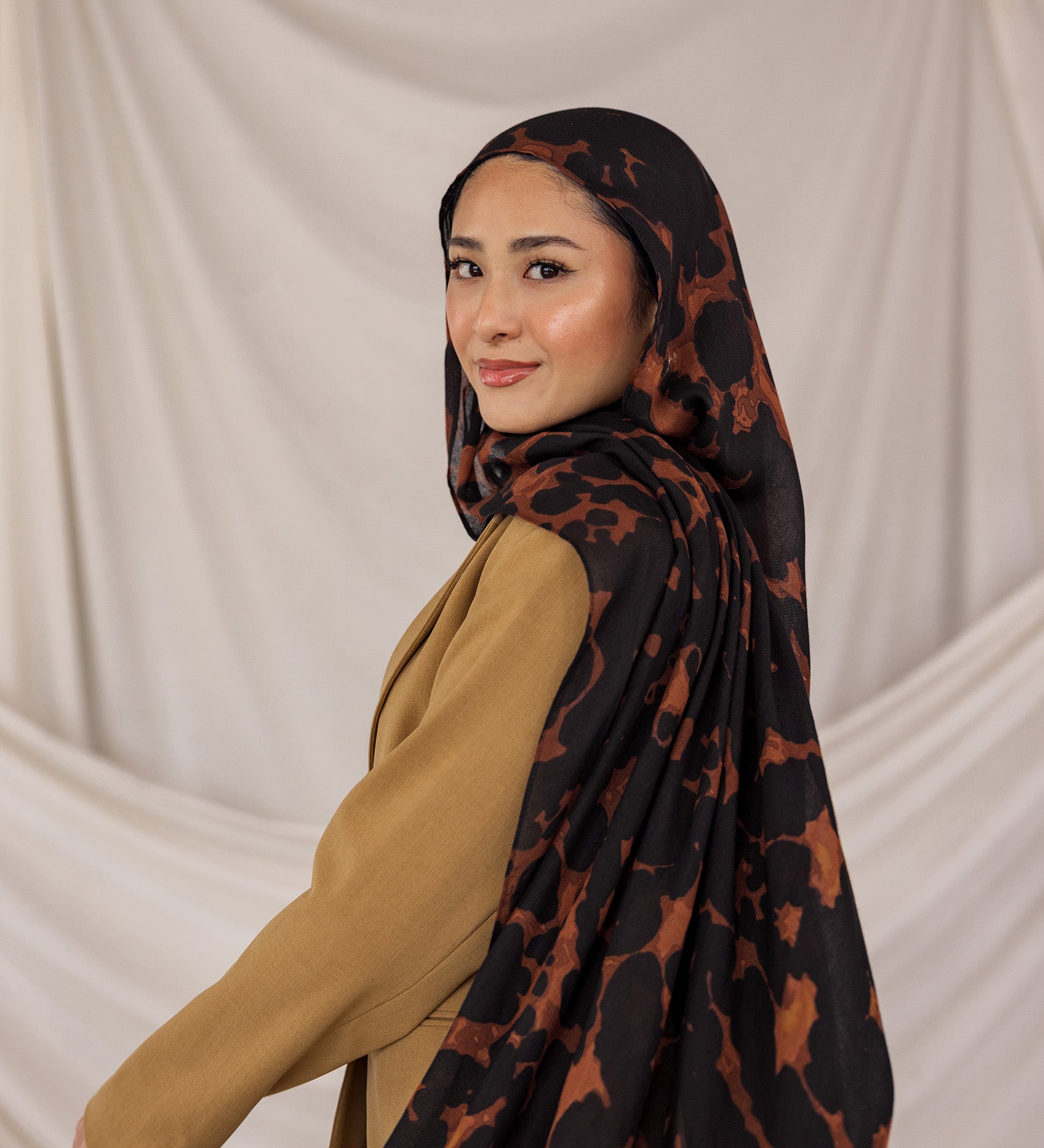 Model wearing a black and brown tortoiseshell patterned hijab against a plain background