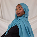 Person wearing a bright blue hijab against a plain background