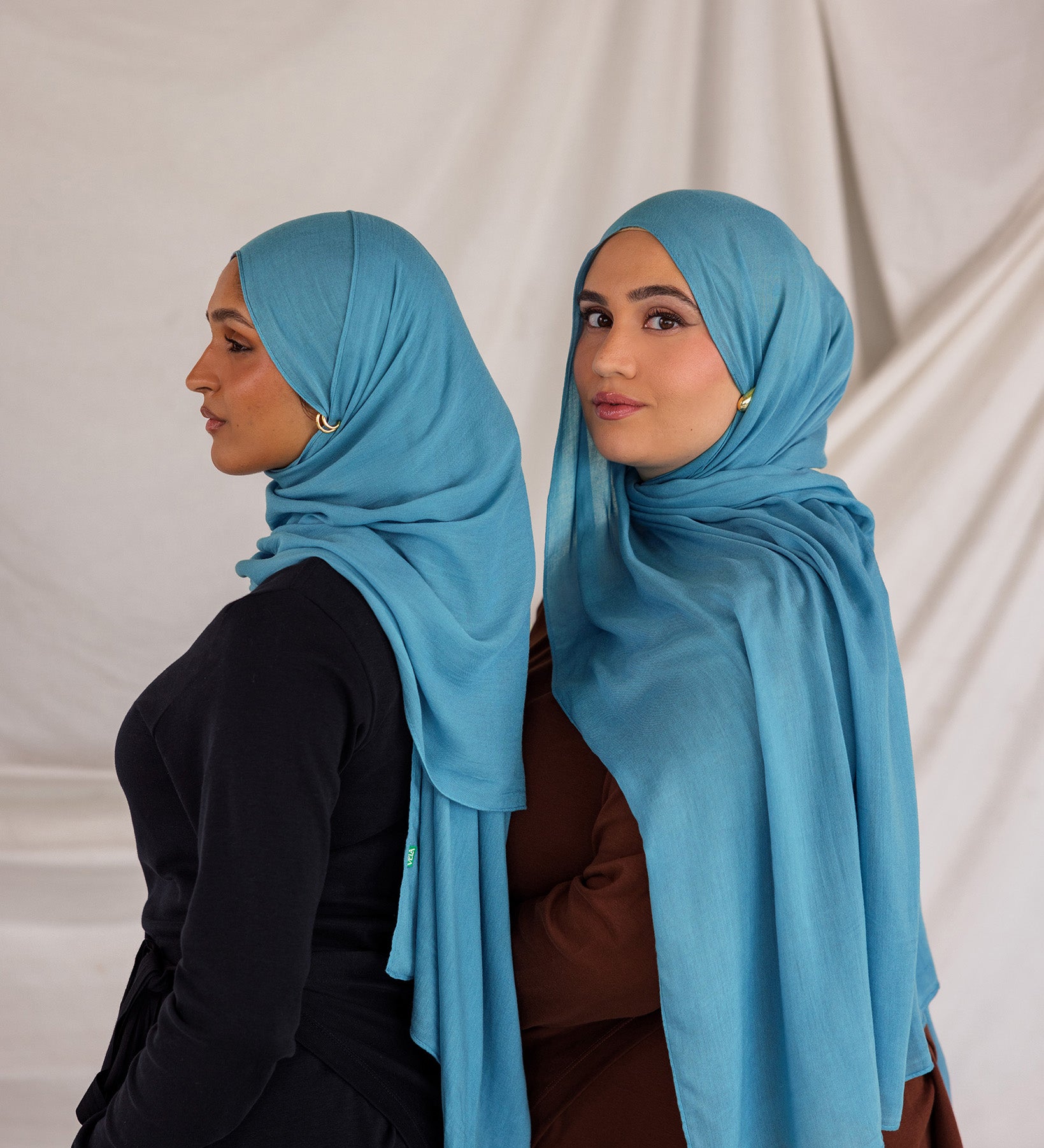 Two models styled in bright blue hijabs against a plain background
