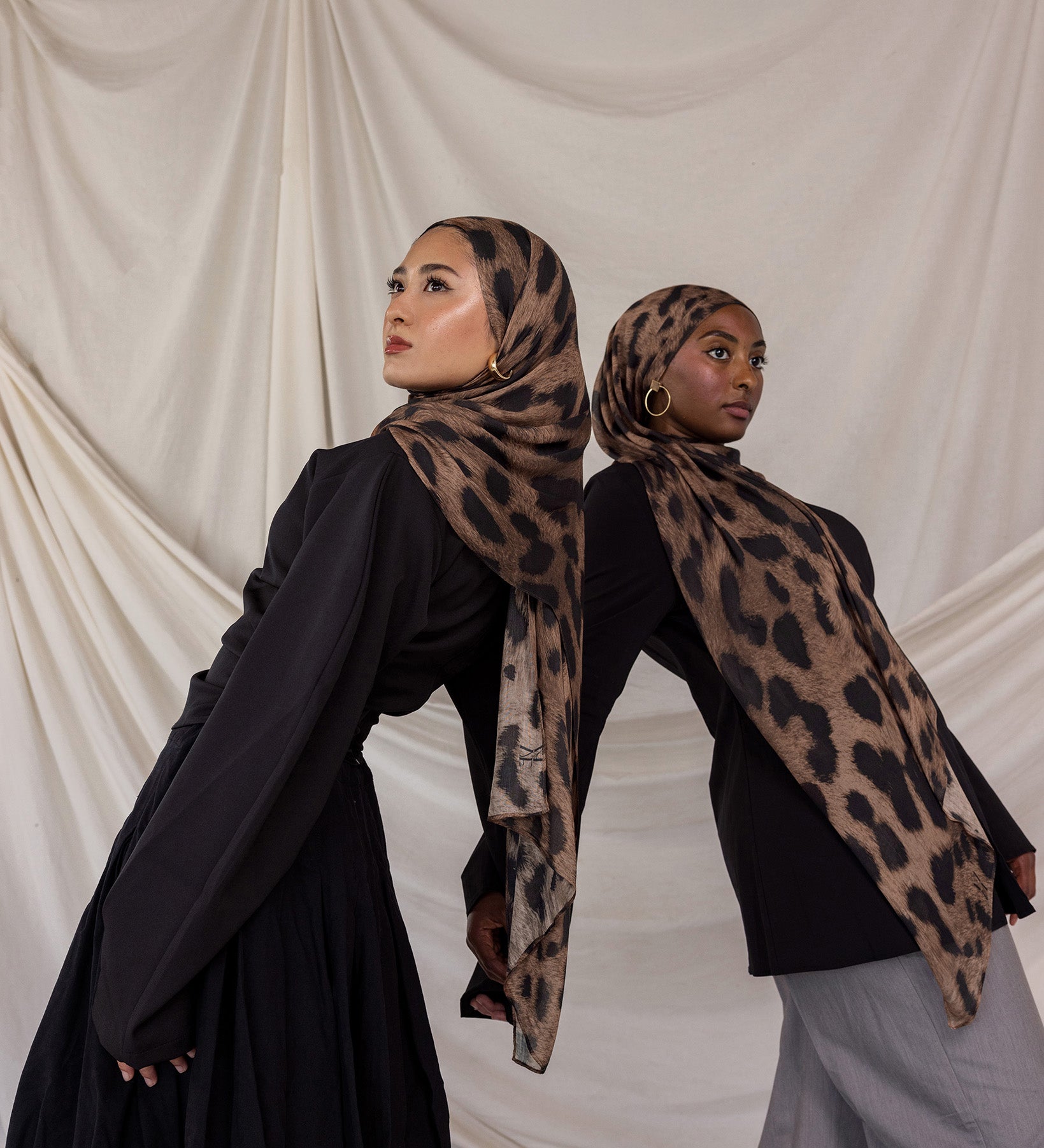 Two women wearing brown leopard print hijabs against a plain background