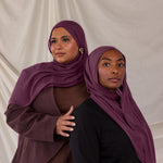 Two models styled in purple red hijabs against a plain background