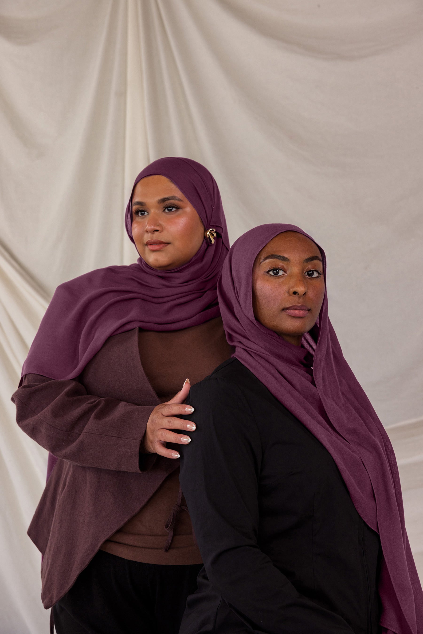 Two models styled in purple red hijabs against a plain background