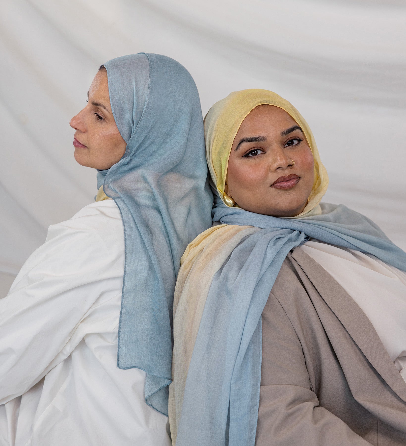 Two girls wearing hijabs in light blue and yellow gradient against a plain background