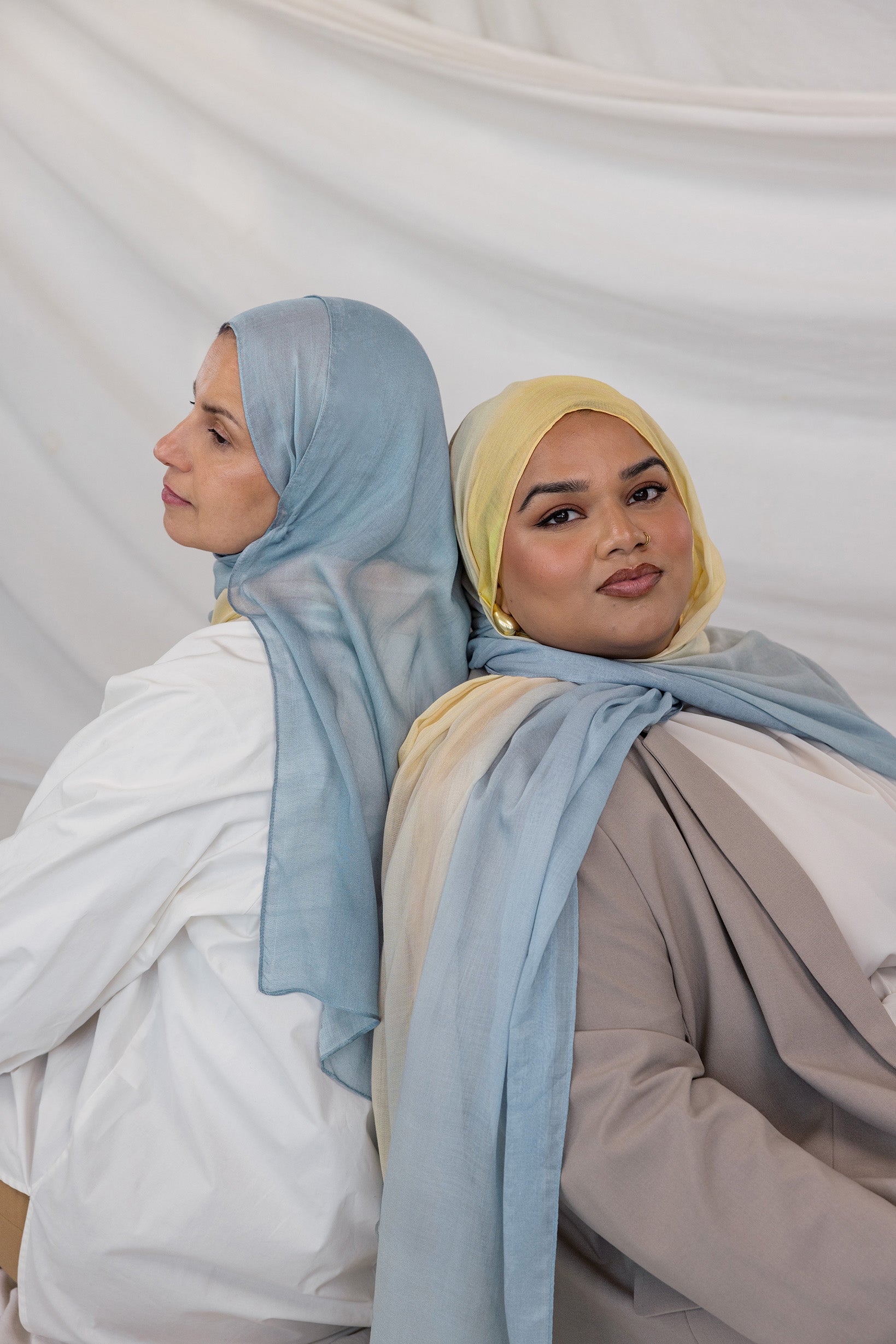 Two girls wearing hijabs in light blue and yellow gradient against a plain background