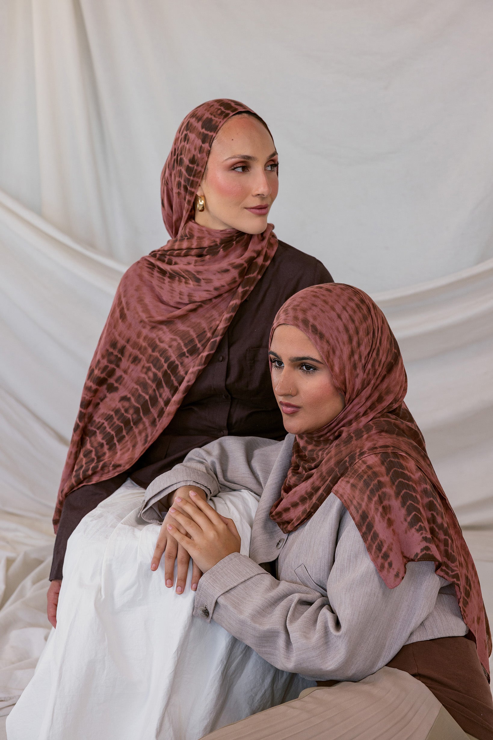 Two women wearing red clay ripple printed hijabs sitting against a plain background