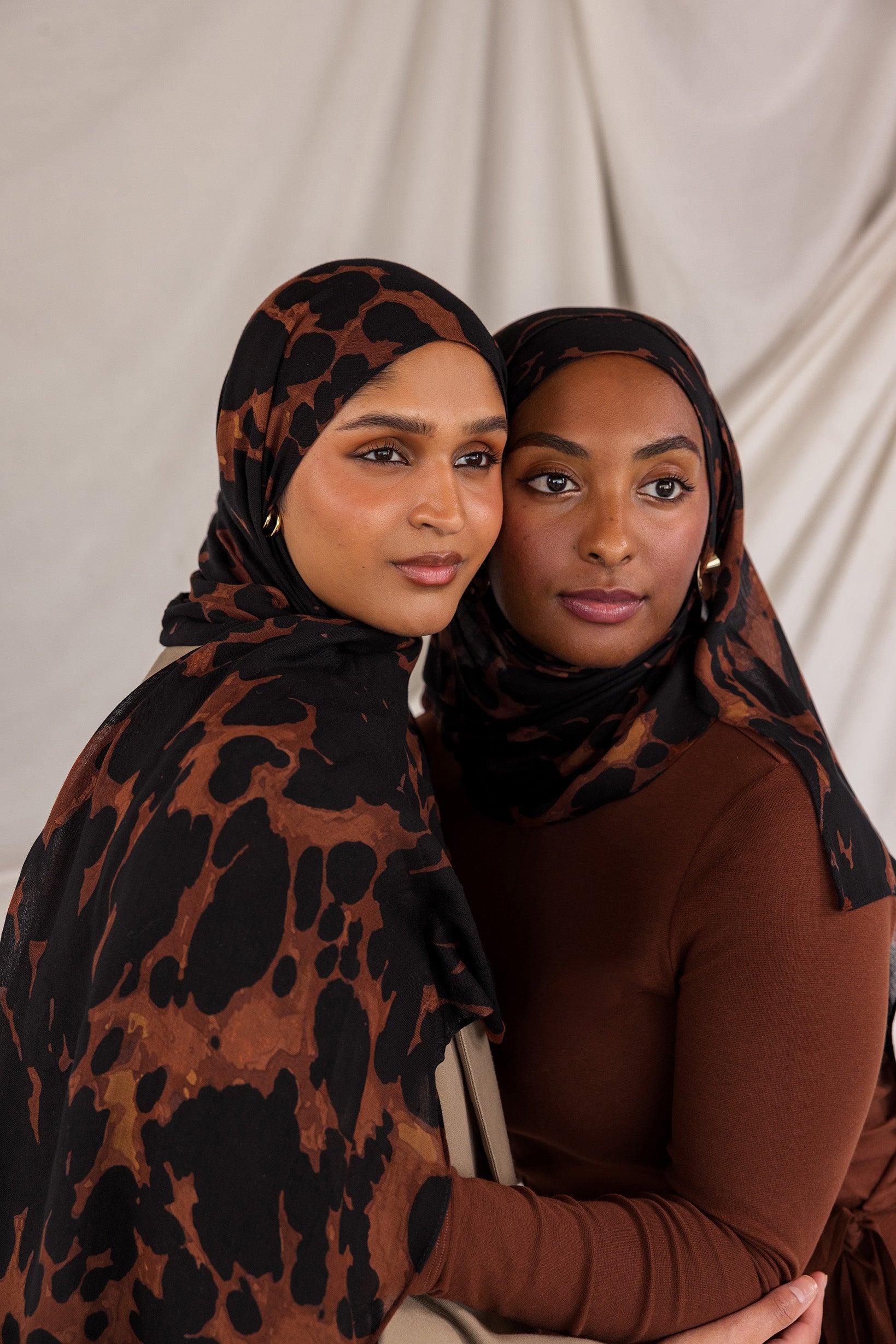 Two women styled in tortoiseshell patterned hijabs against a plain background