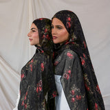 Two women wearing black pomegranate printed hijabs against a plain background