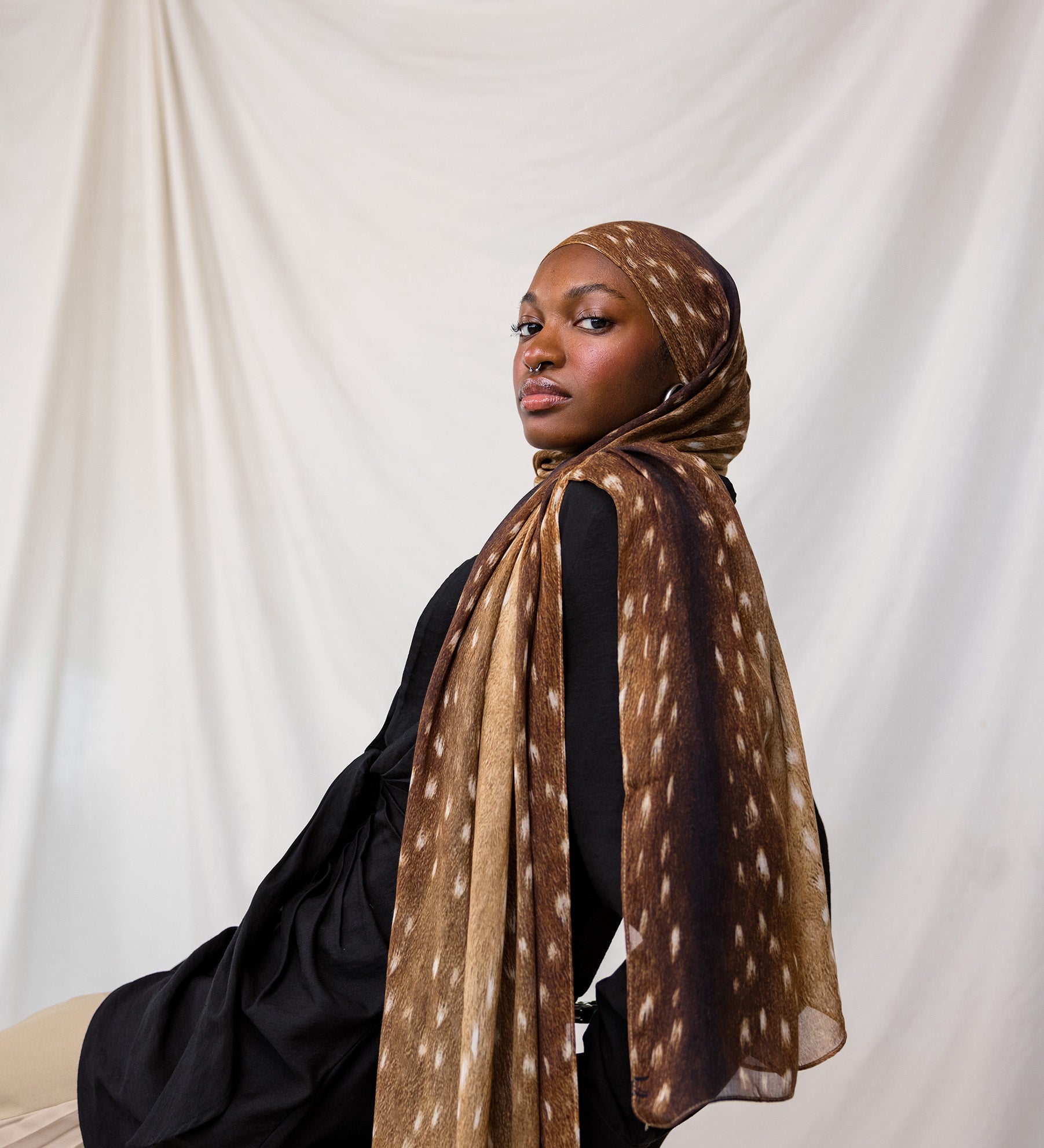 Fawn print depicted styled on model, this scarf features warm brown tones with white spots that resemble a fawn print.