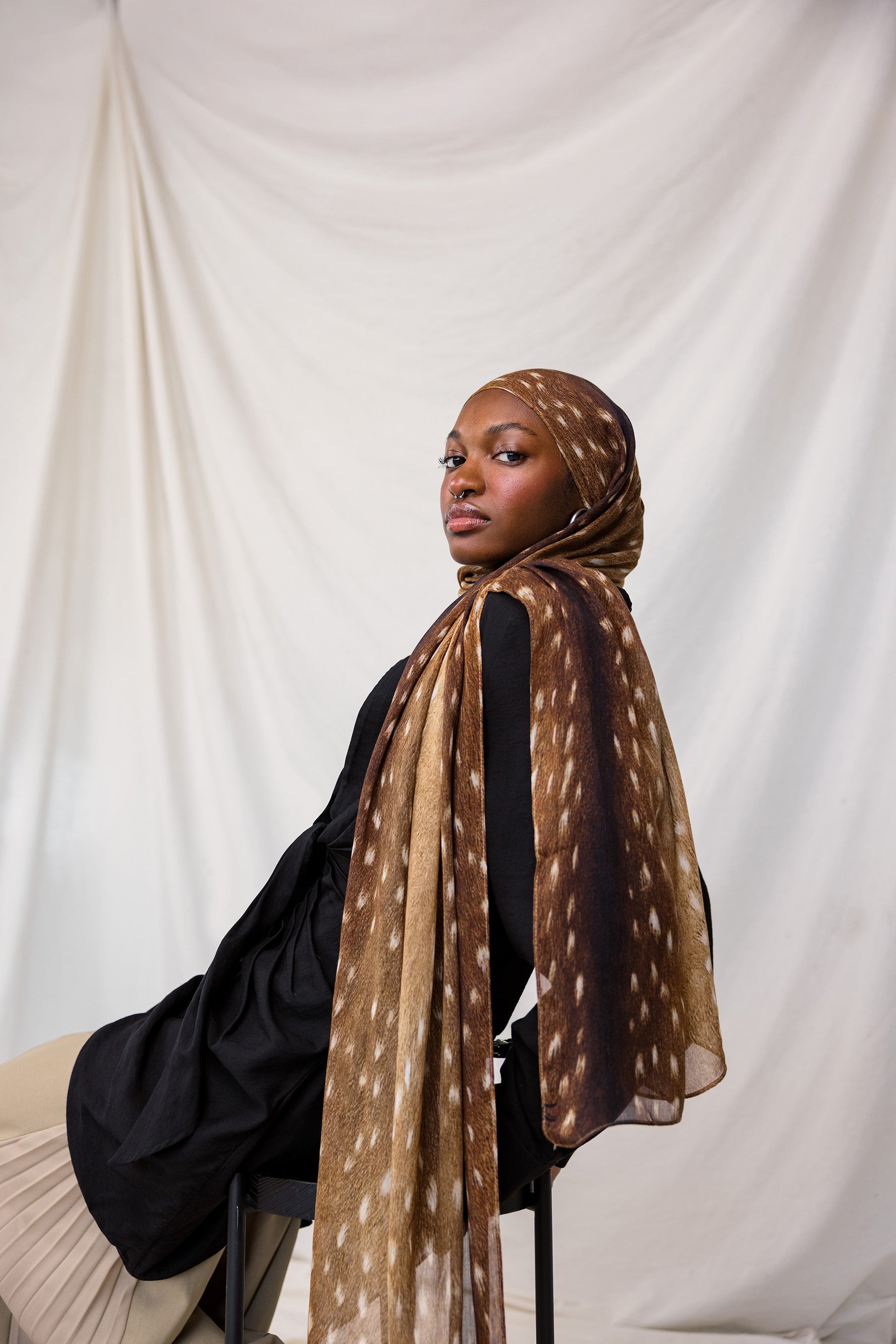 Fawn print depicted styled on model, this scarf features warm brown tones with white spots that resemble a fawn print.