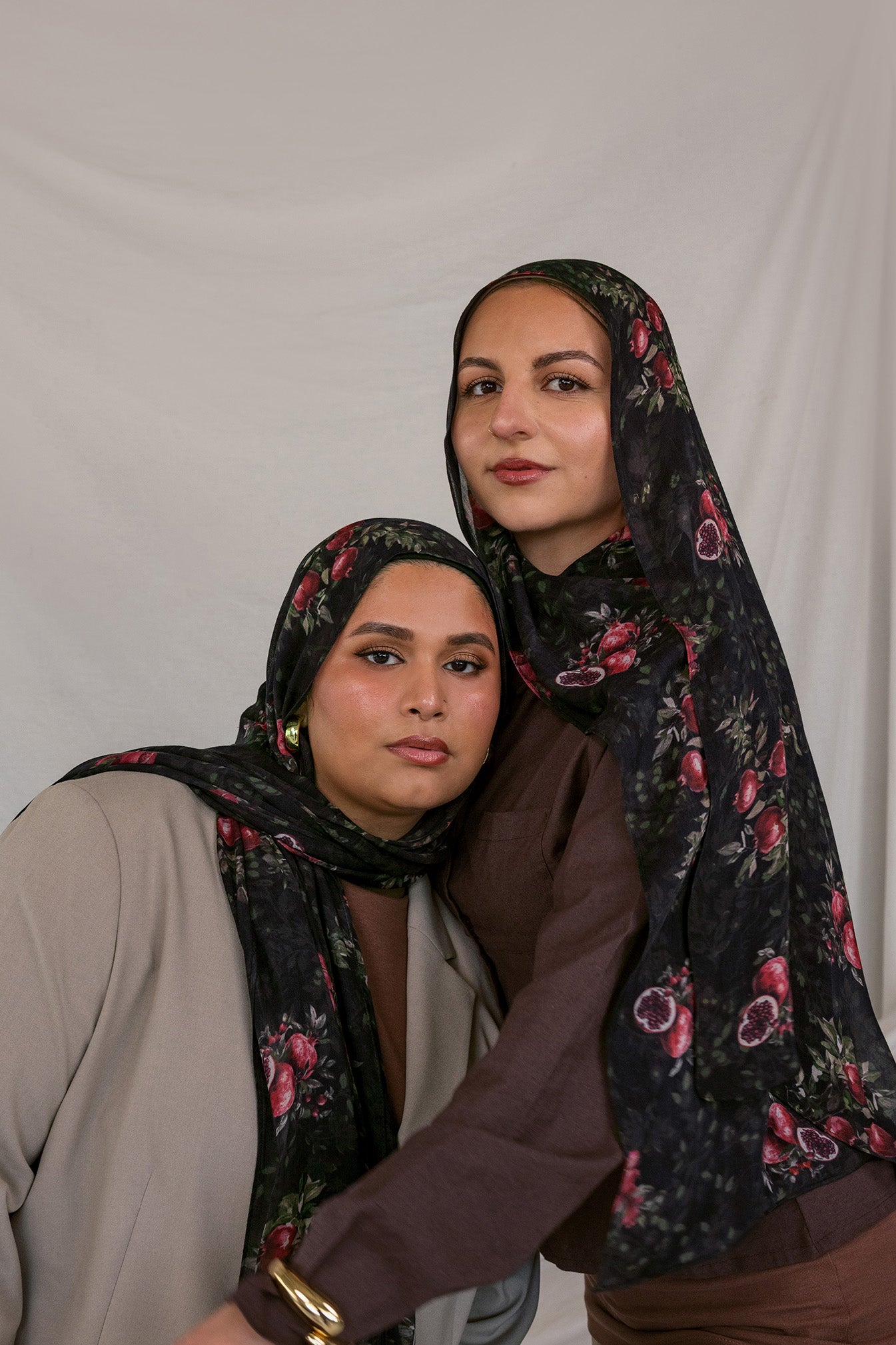 Two models wearing black pomegranate printed hijabs against a plain background