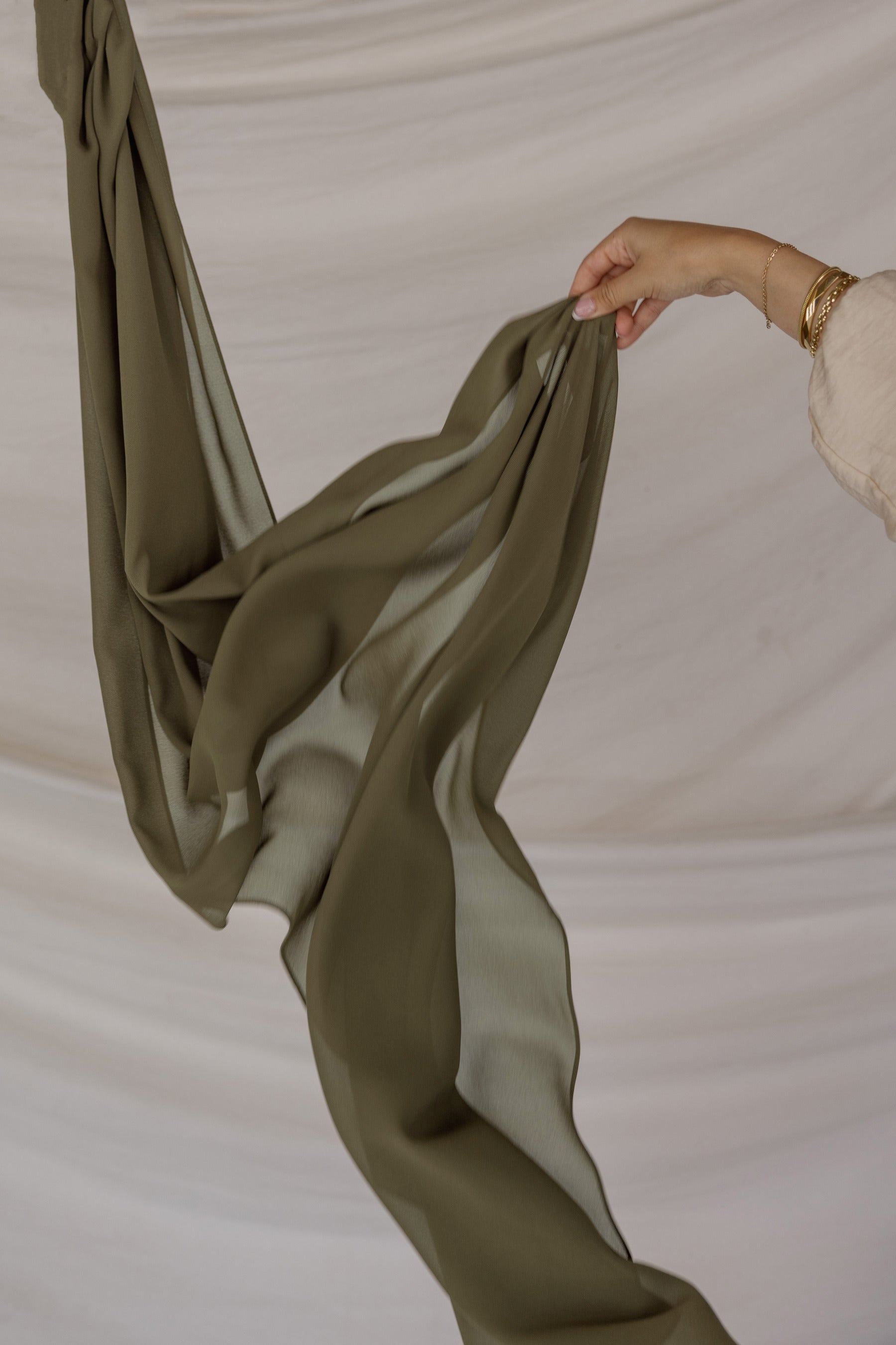 Green chiffon hijab being held against a neutral background