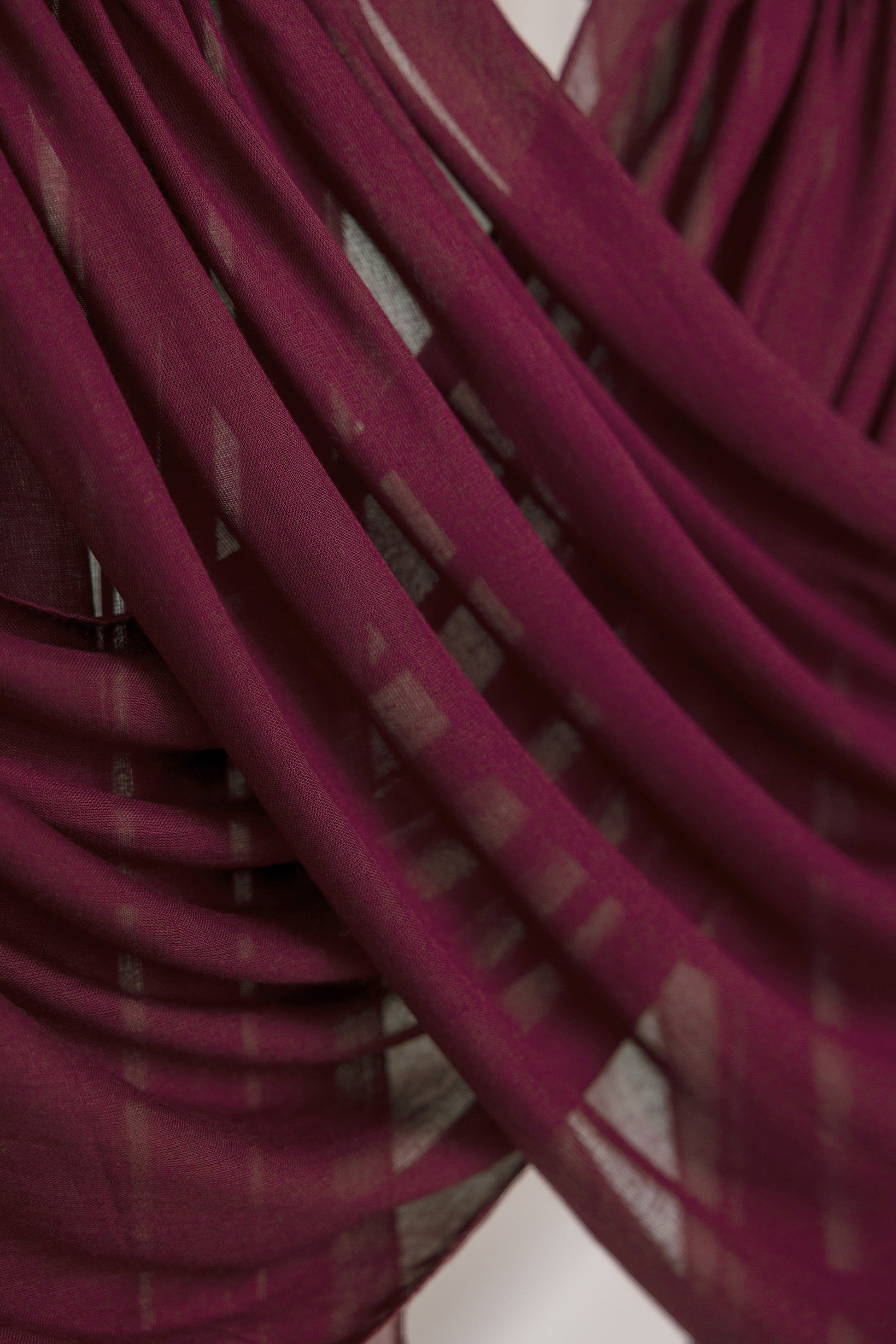 Maroon hijab suspended and gently draped to show the lightweight fabric and texture in soft lighting.