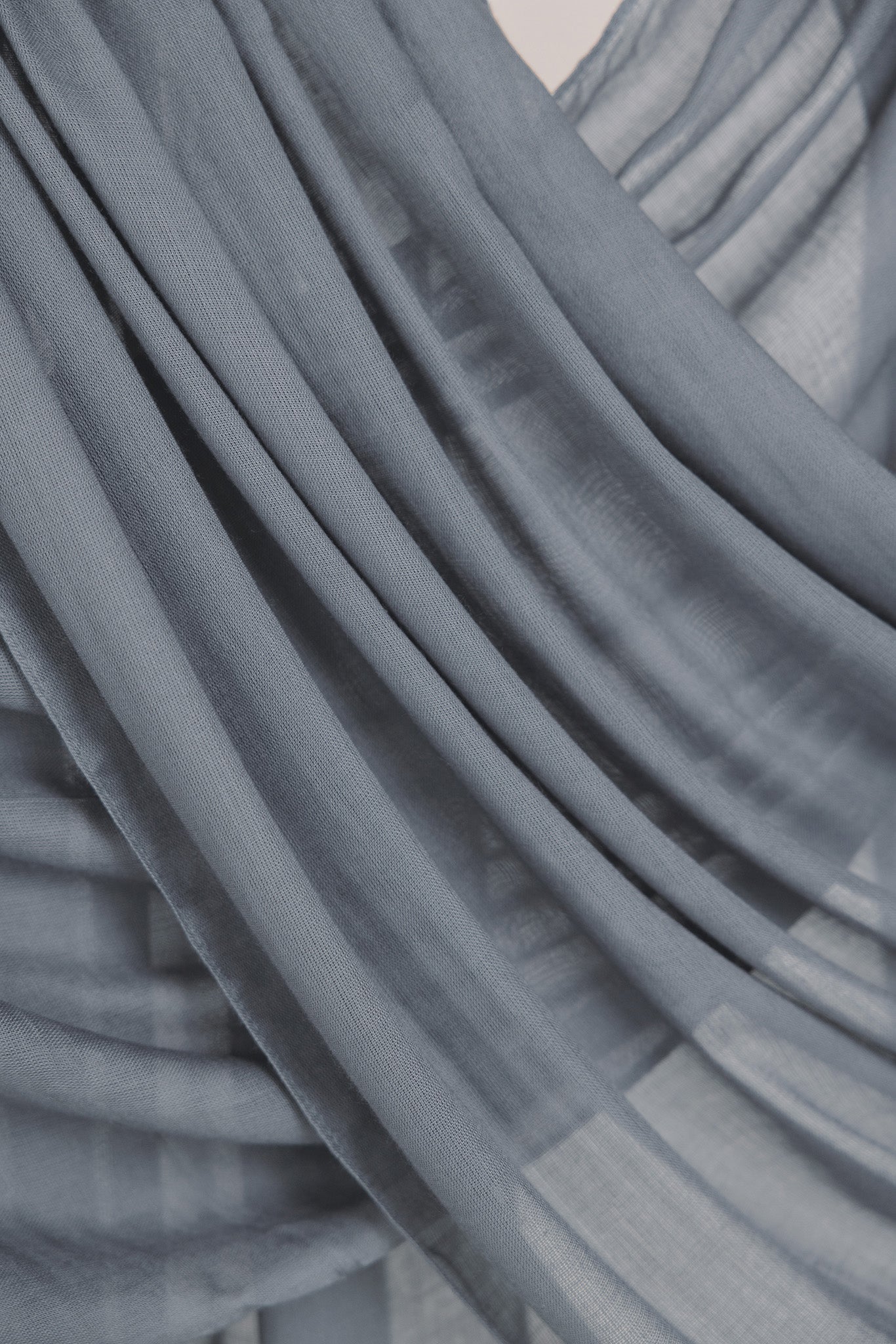Close-up of draping folds of the dark sage hijab over a neutral backdrop.