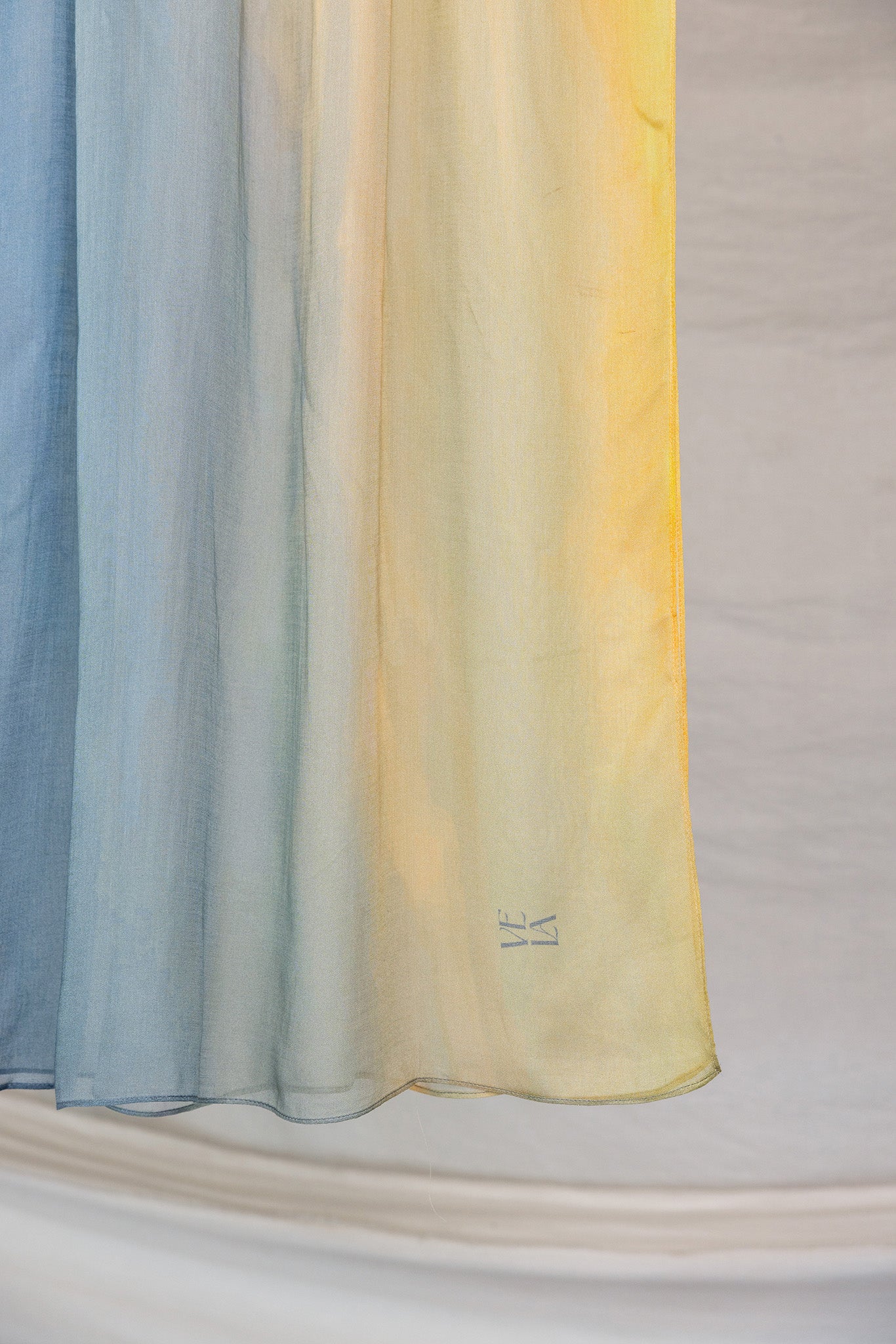 Close up of yellow to blue ombre hijab draped in front of white background