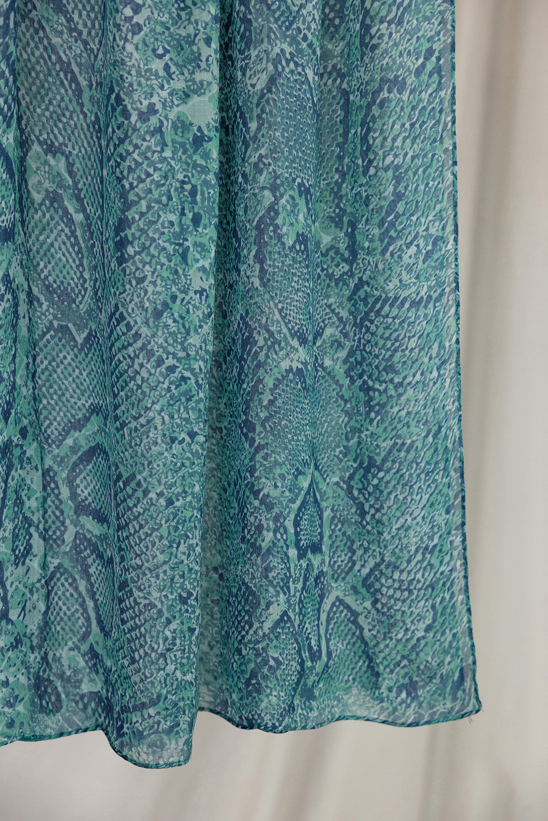 A close-up product shot of the Aqua Cobra scarf that features blue and teal scale-like designs.