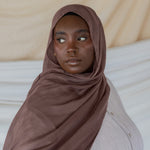 Model wearing taupe colored hijab against backdrop.