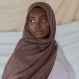 Model wearing taupe colored hijab against backdrop.