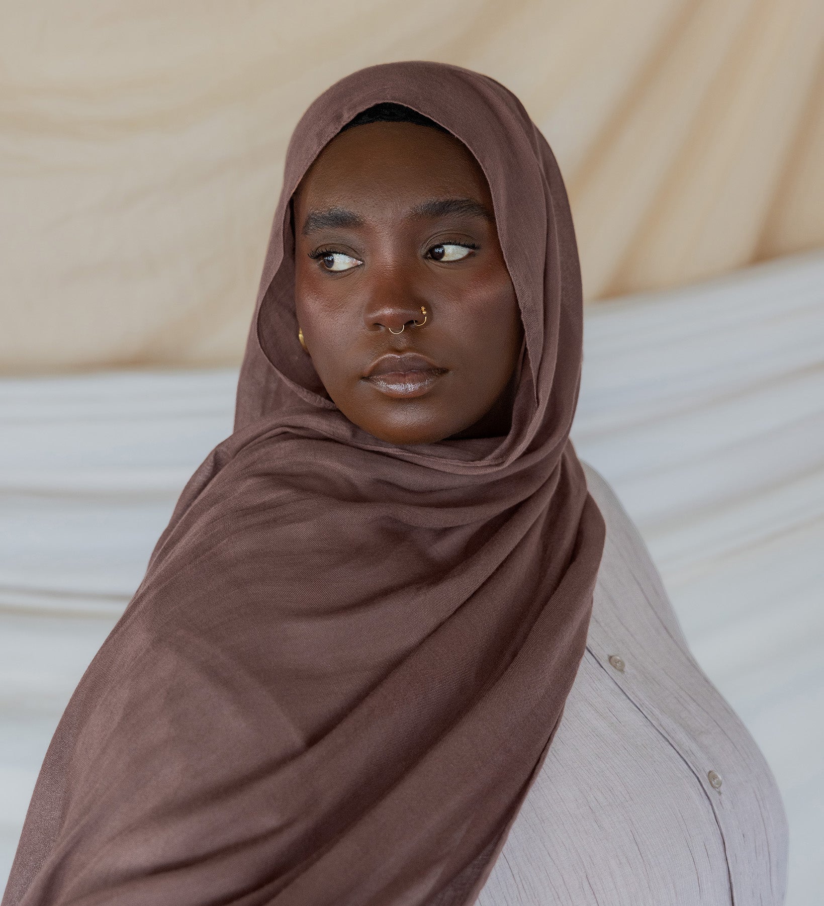 Model wearing taupe colored hijab against backdrop.