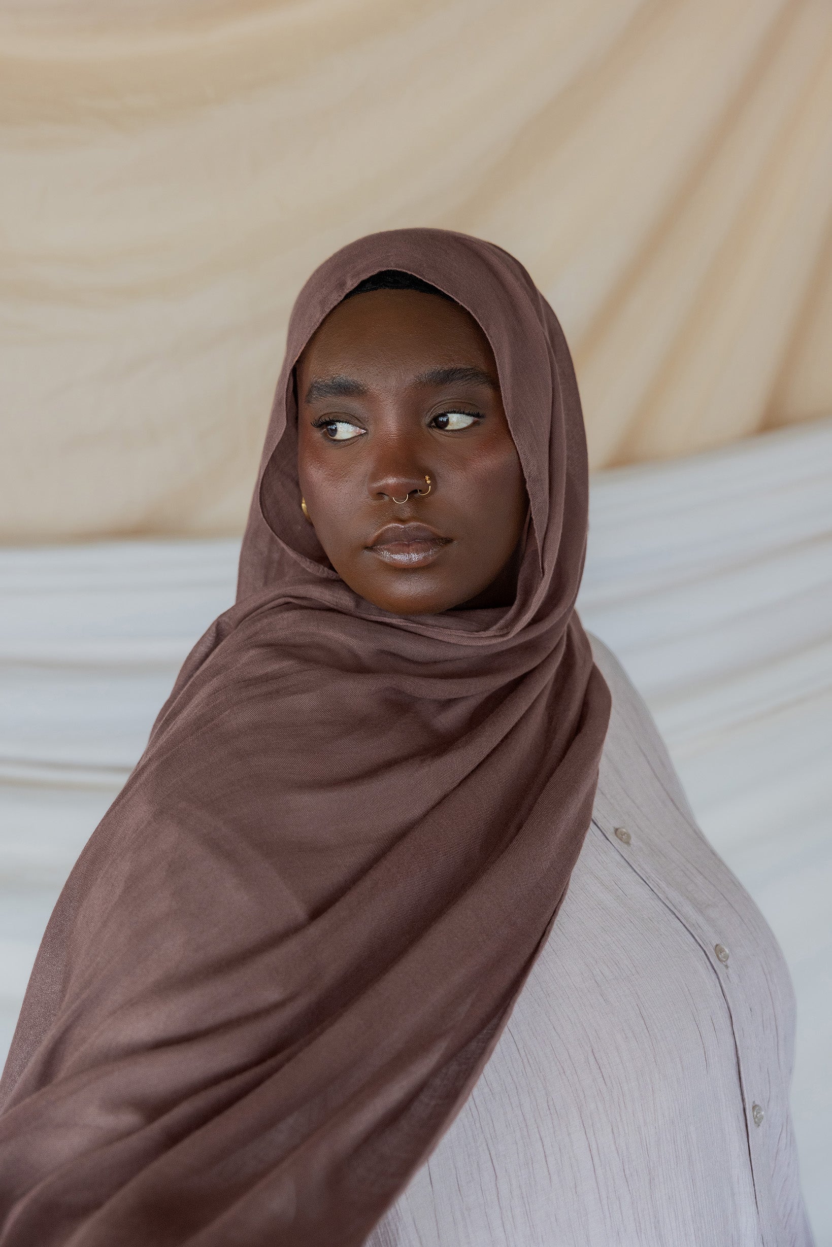 Model wearing taupe colored hijab against backdrop.