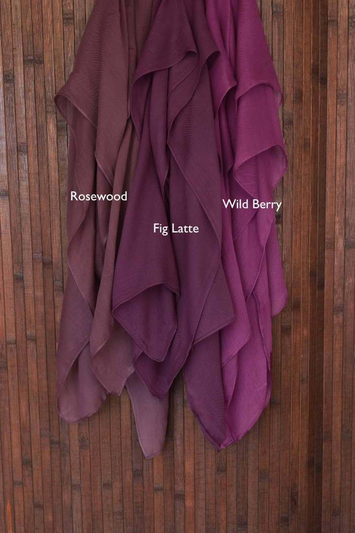 Color comparison of three purple red hijab fabrics labeled 'Rosewood', 'Wild Berry', and 'Fig Latte' on a wooden background.