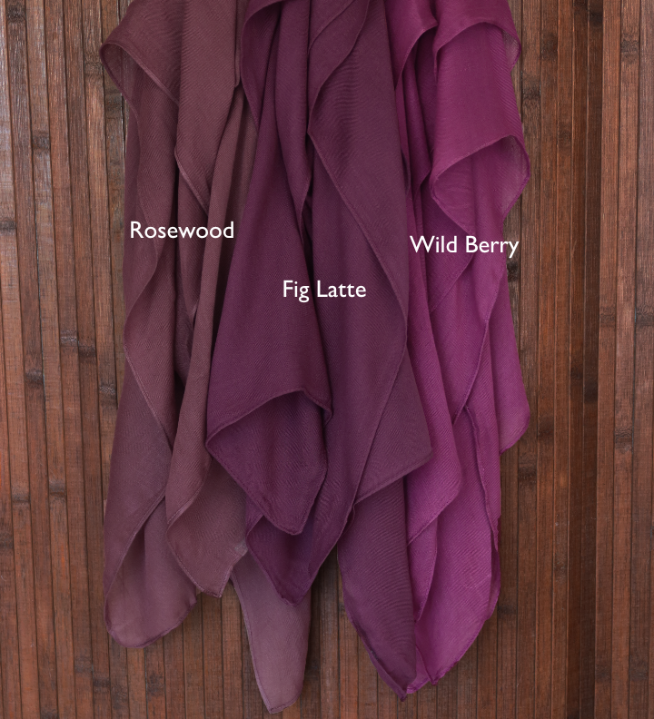 Color comparison of three purple red hijab fabrics labeled 'Rosewood', 'Wild Berry', and 'Fig Latte' on a wooden background.