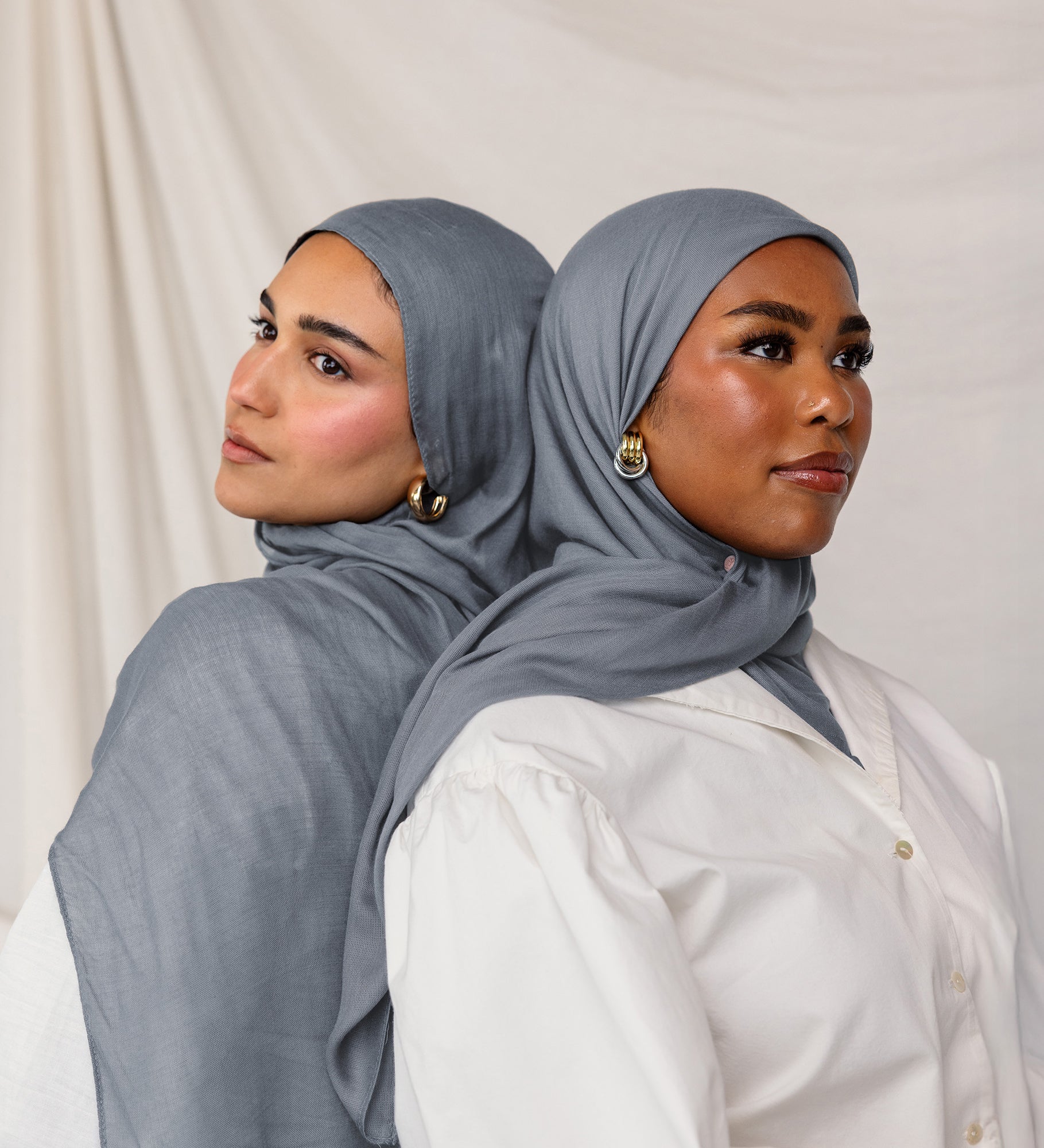Head-and-shoulders of two models side by side, each wearing the dark sage hijab with one in front and the other in slight profile.