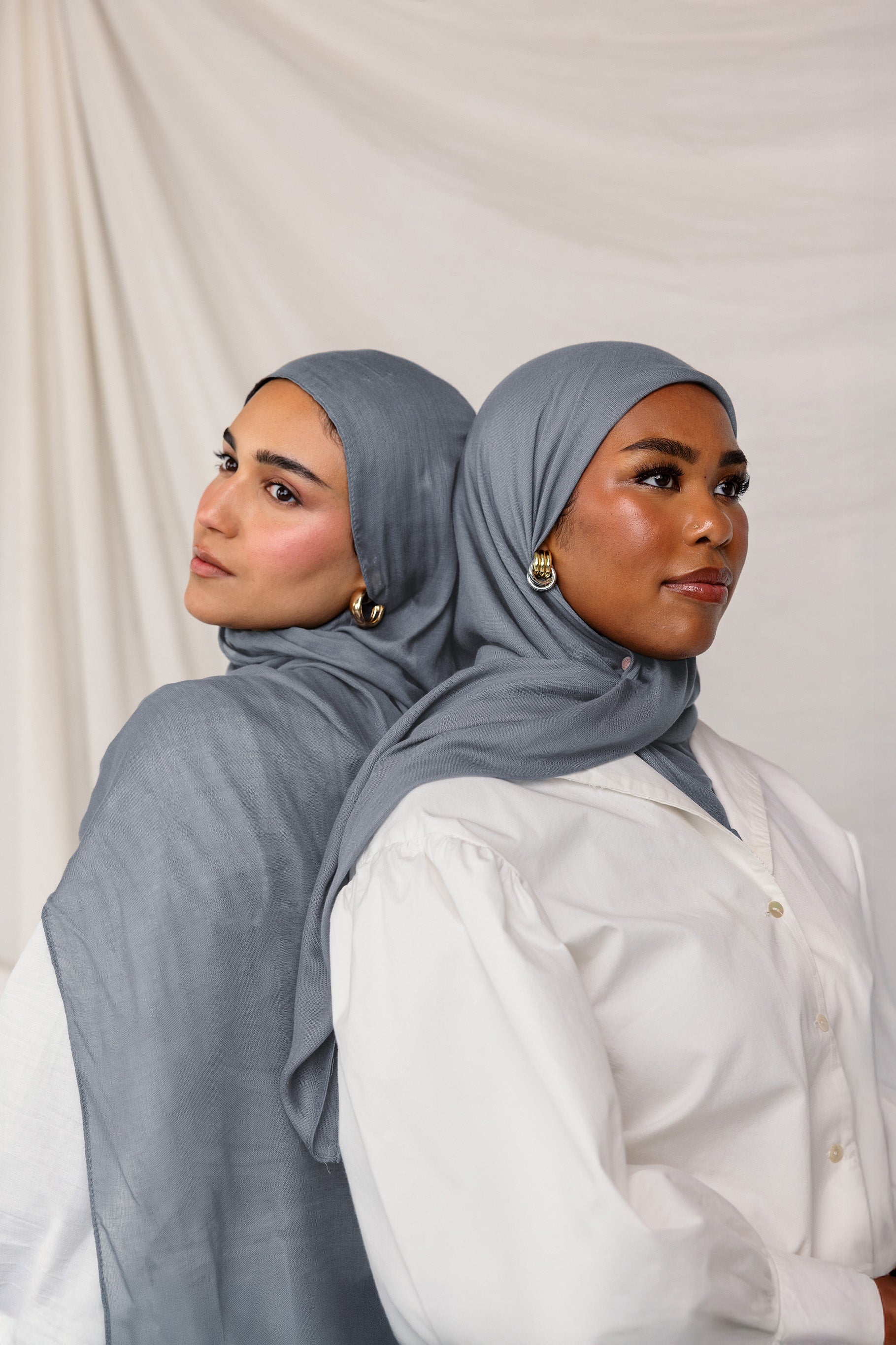 Head-and-shoulders of two models side by side, each wearing the dark sage hijab with one in front and the other in slight profile.