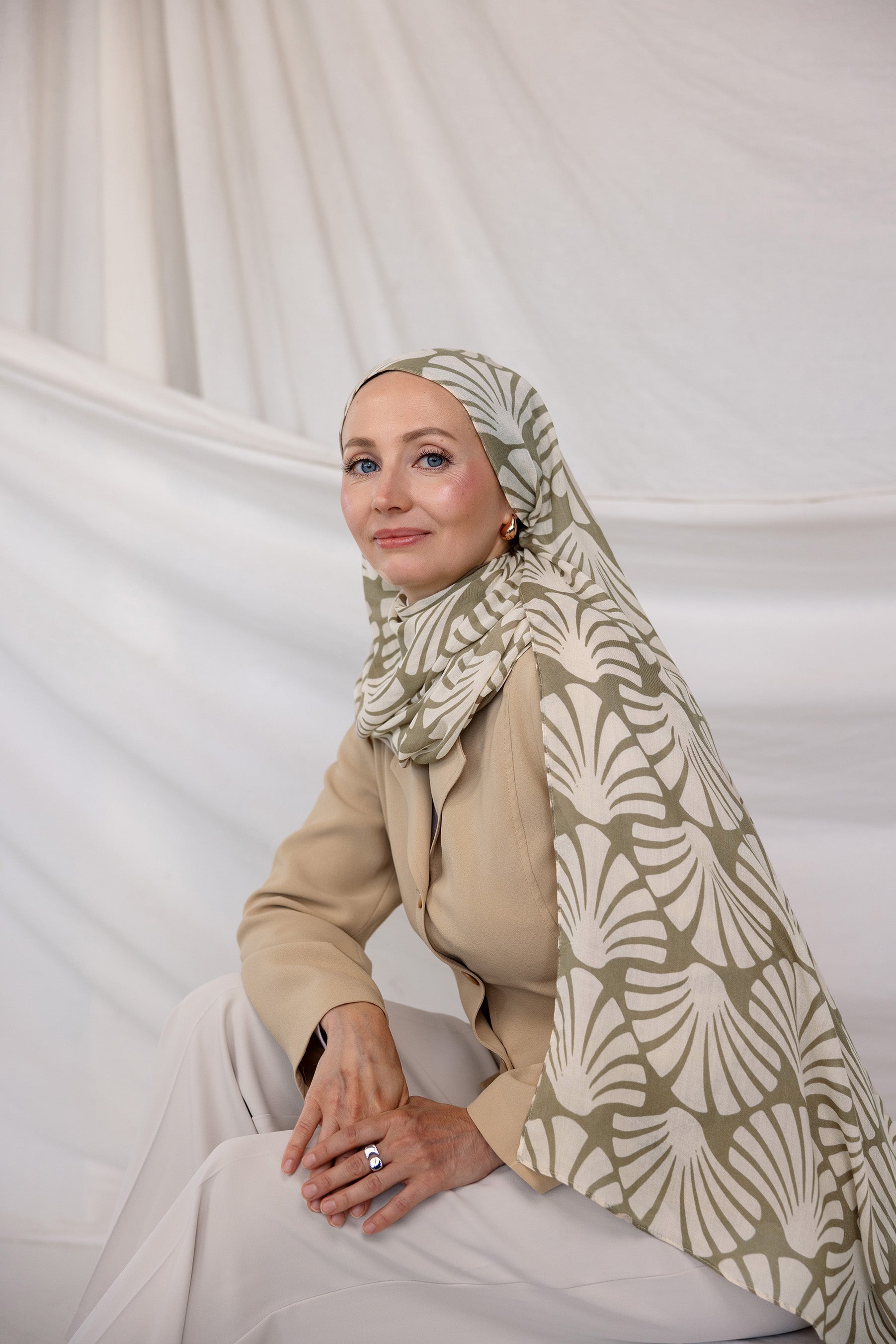 Woman wearing a patterned Sand Shells hijab and beige outfit against a white background