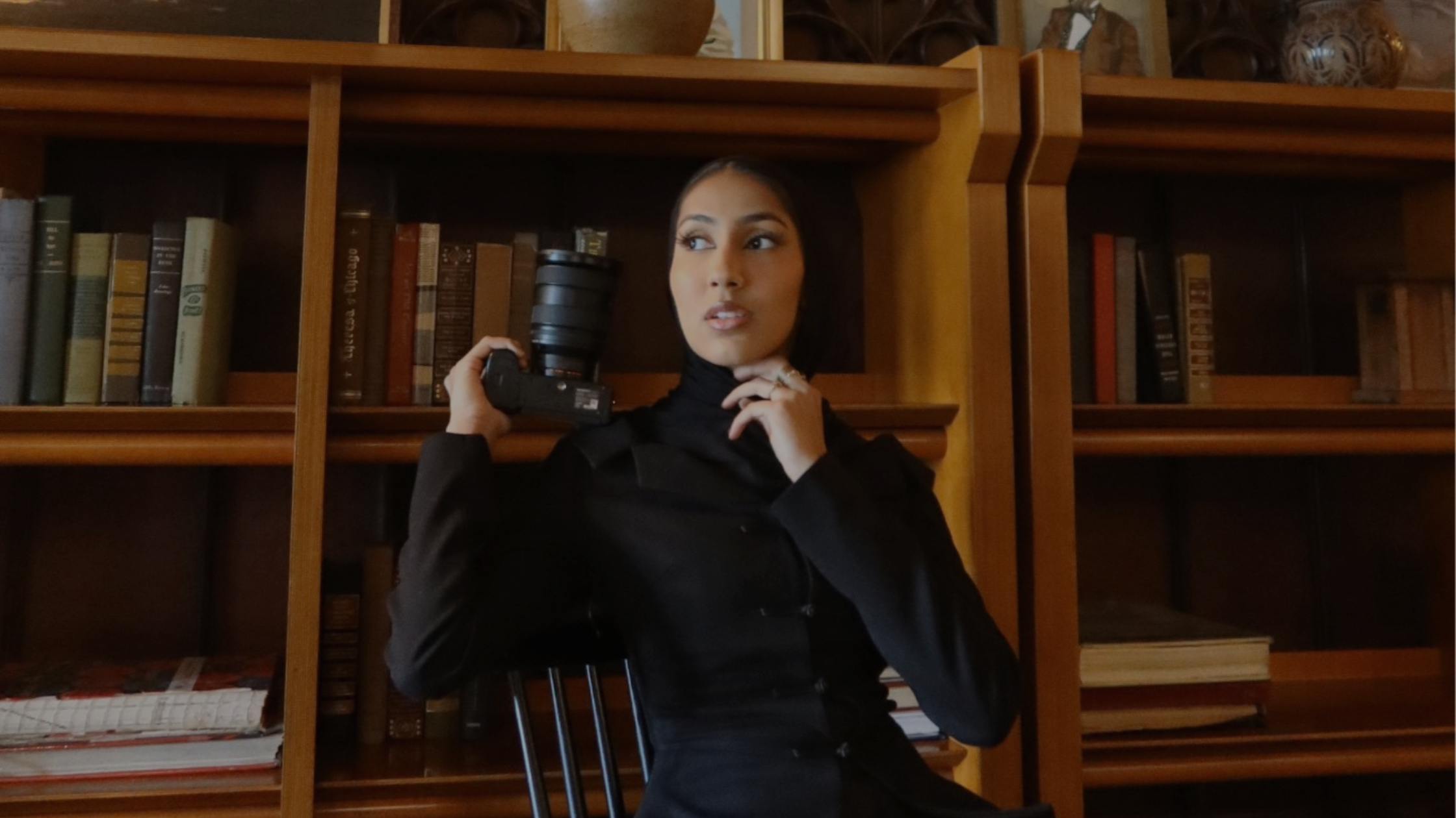 A girl in a black headscarf posing while holding a camera.