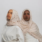 Two women wearing polka dot buttercream hijabs and white tops against a plain background