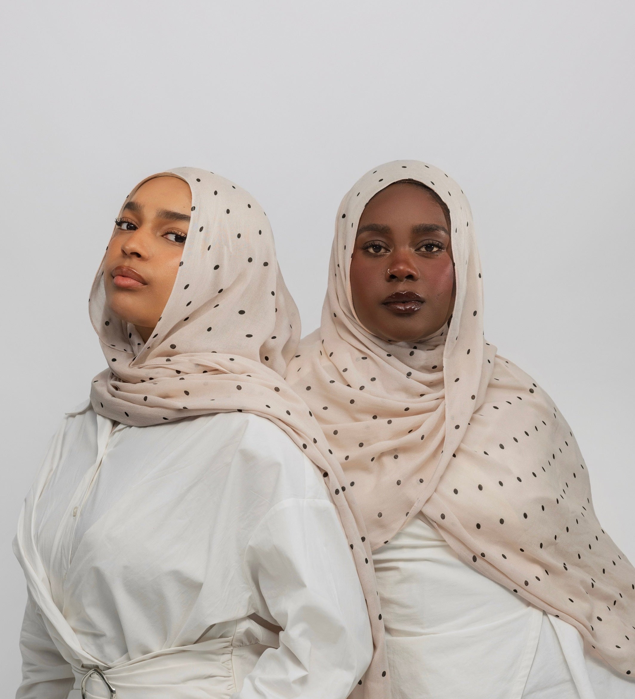 Two women wearing polka dot buttercream hijabs and white tops against a plain background