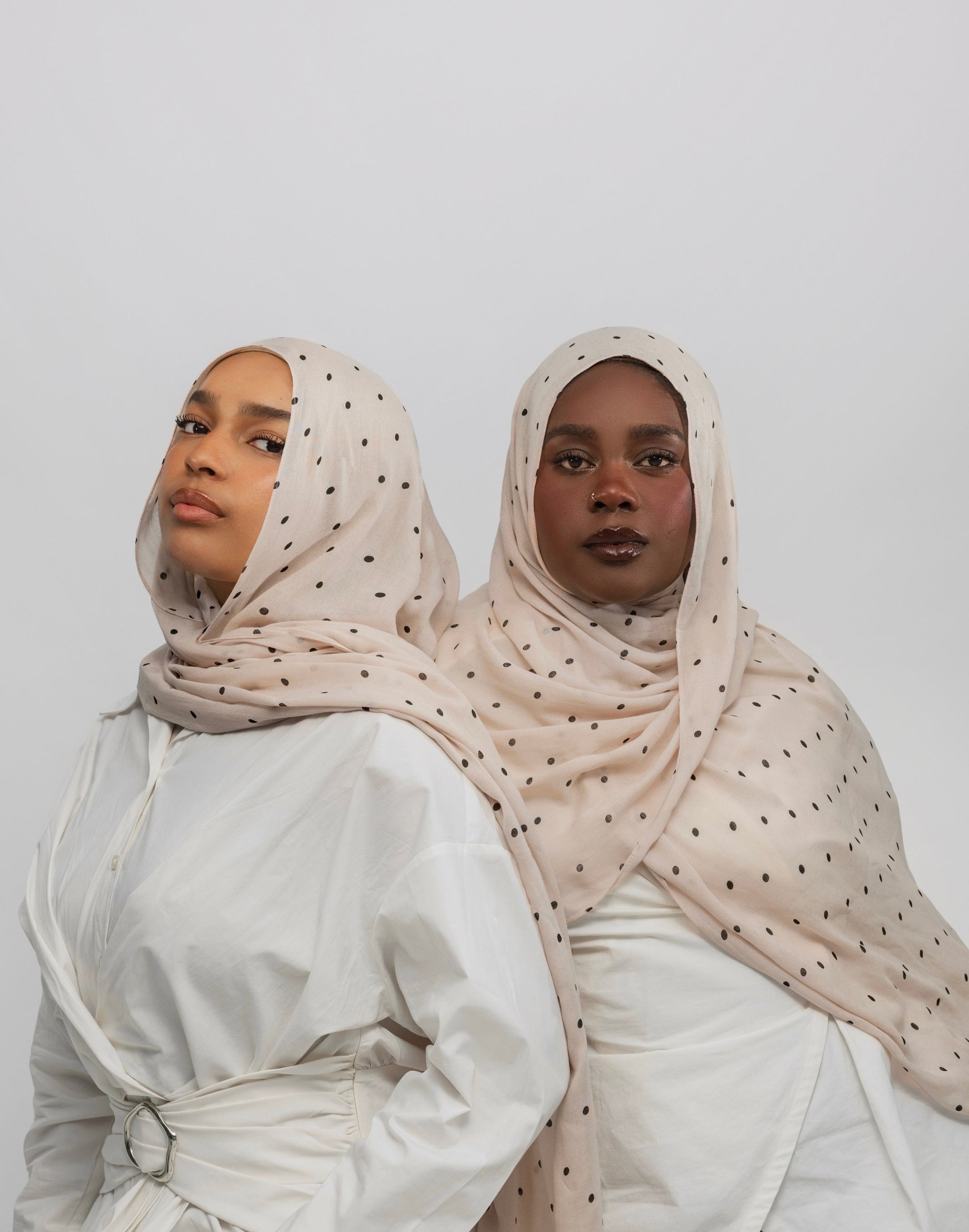 Two women wearing polka dot buttercream hijabs and white tops against a plain background