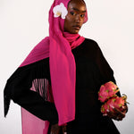Woman wearing a bright pink hijab with a white flower, holding dragon fruit, on a light gray background