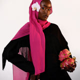 Woman wearing a bright pink hijab with a white flower, holding dragon fruit, on a light gray background