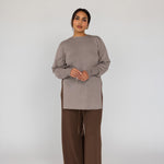 Woman wearing a beige top and brown pants on a white background