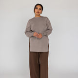 Woman wearing a beige top and brown pants on a white background