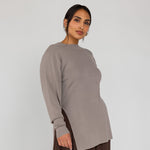 Woman wearing a long-sleeve beige top and brown pants on a white background