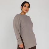 Woman wearing a long-sleeve beige top and brown pants on a white background