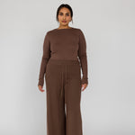 Model styled in a brown outfit with wide-leg pants on a white background