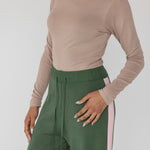 Person wearing a beige long-sleeve top and green pants with pink stripes on a white background