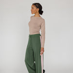 Woman wearing a beige top and green pants with pink stripes on a white background