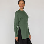 Woman wearing a green knit top and black pants on a white background