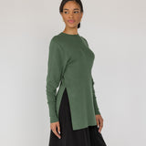 Woman wearing a green knit top and black pants on a white background